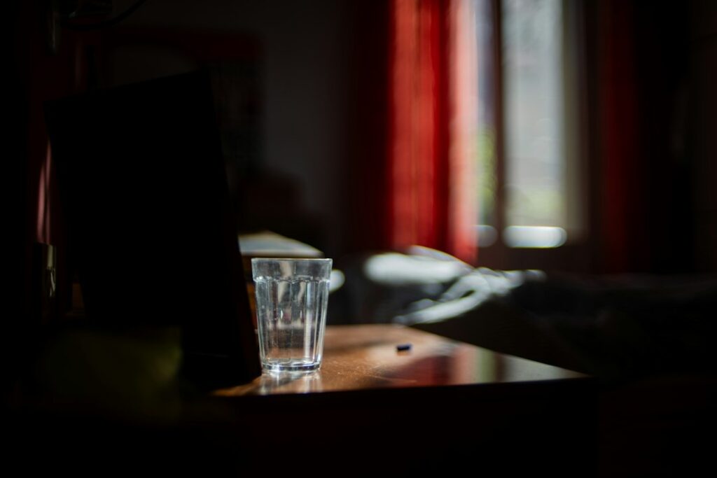 A tired adult sits at home drinking water beside a glass and a reusable bottle.